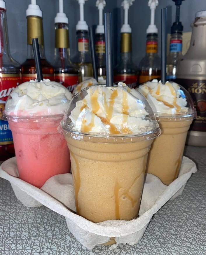 Three blended drinks, including strawberry and caramel flavors, in a to-go tray