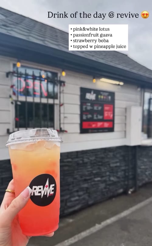 Hand holding an orange energy spritzer drink in front of the Revive Coffee Stand window